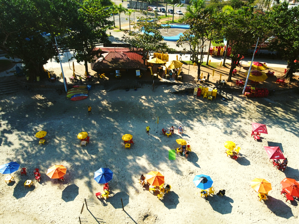 Vista aérea do quiosque com mesas ecadeiras na areia da Prainha. 